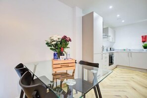 Een moderne keuken met witte kasten, een houten welkomstbord en een glazen tafel met stoelen.
