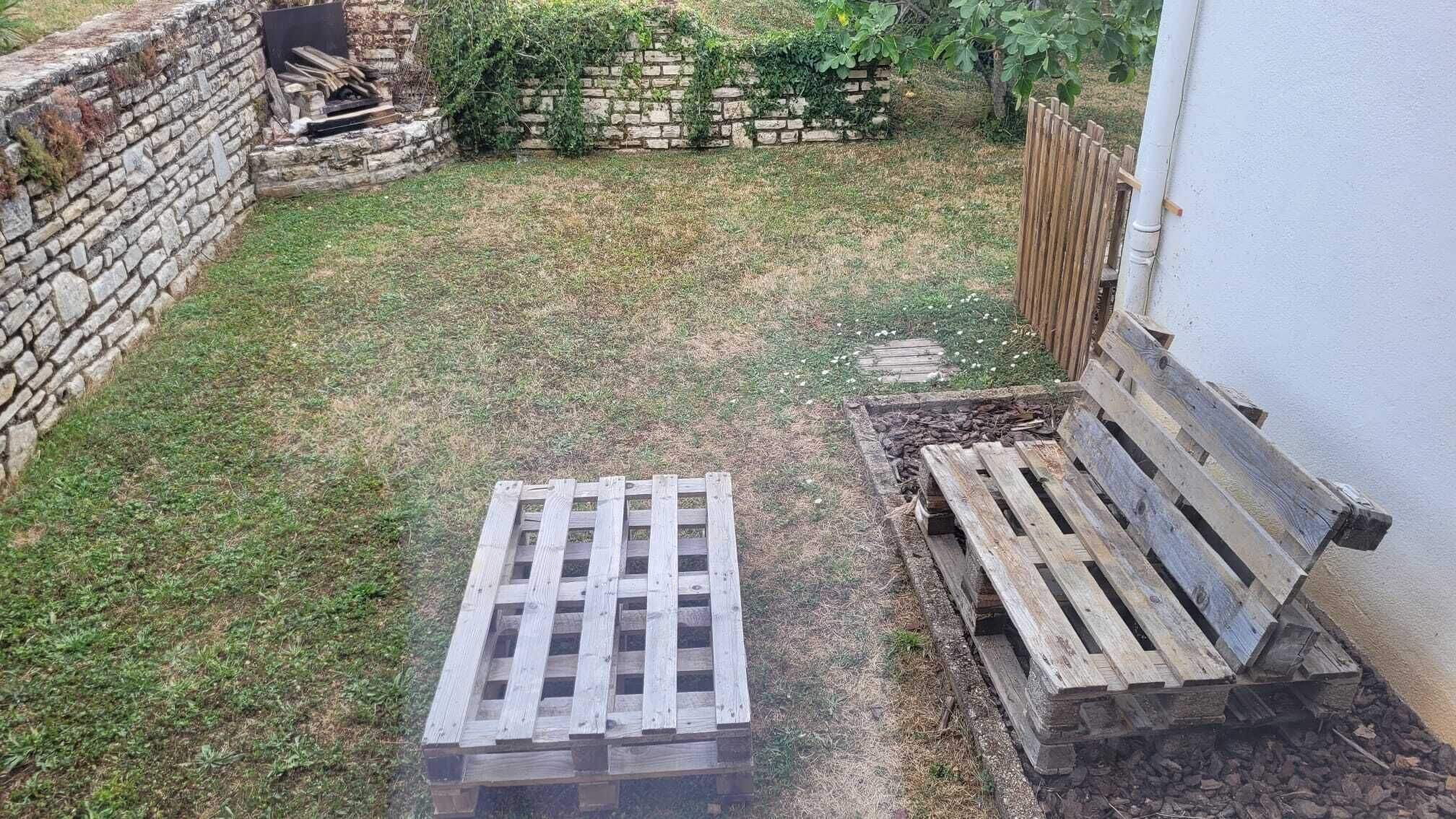 Un muro de piedra, un banco de madera y un palet de madera en un patio.