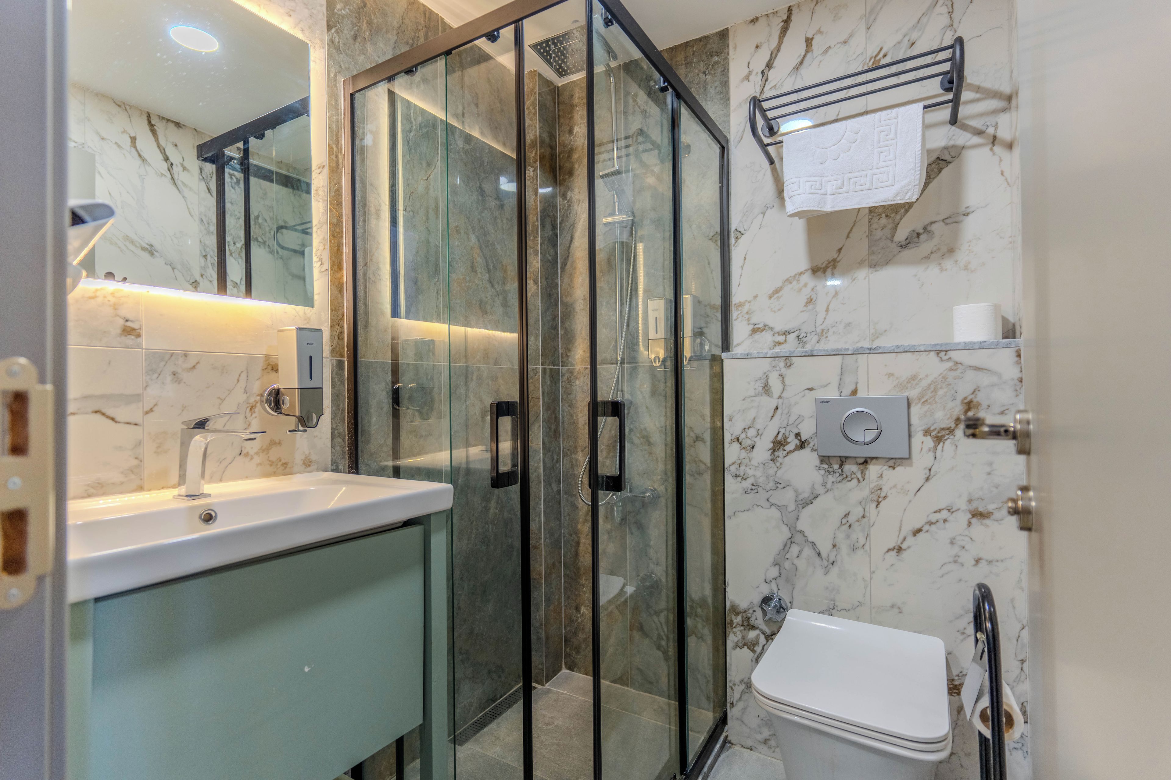 A modern bathroom with a glass-enclosed shower, a sink with a soap dispenser, and a toilet.