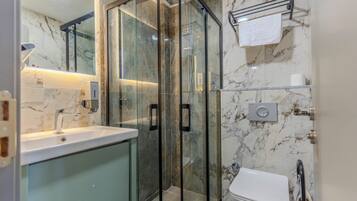 A modern bathroom with a glass-enclosed shower, a sink with a soap dispenser, and a toilet.
