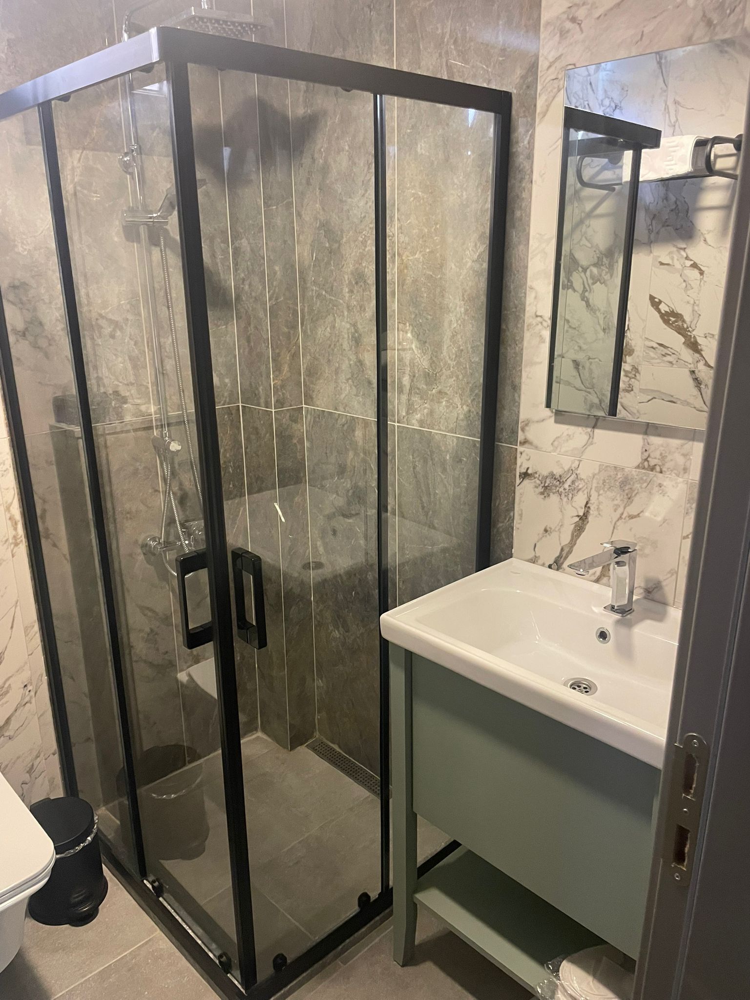 A bathroom with a glass-enclosed shower, a white sink, and a marble-tiled wall.