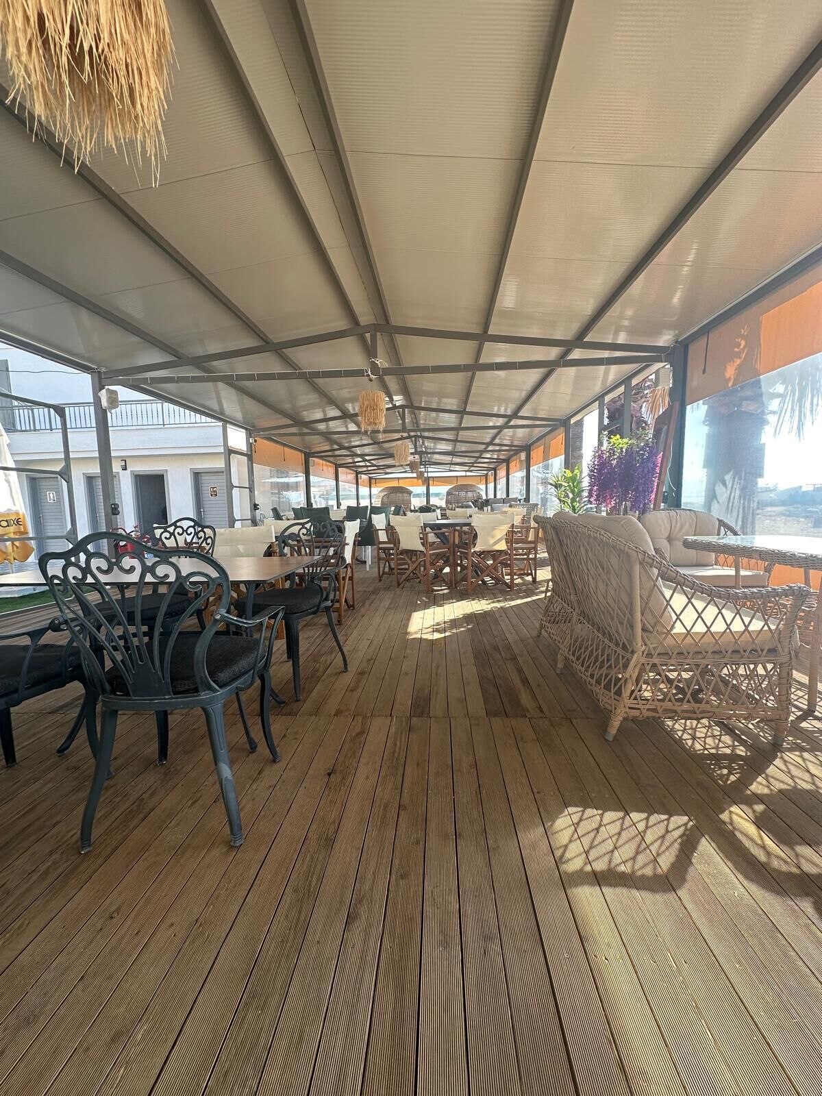 Un espace extérieur aménagé avec un sol en bois, des meubles en métal et en osier, et des décorations suspendues.