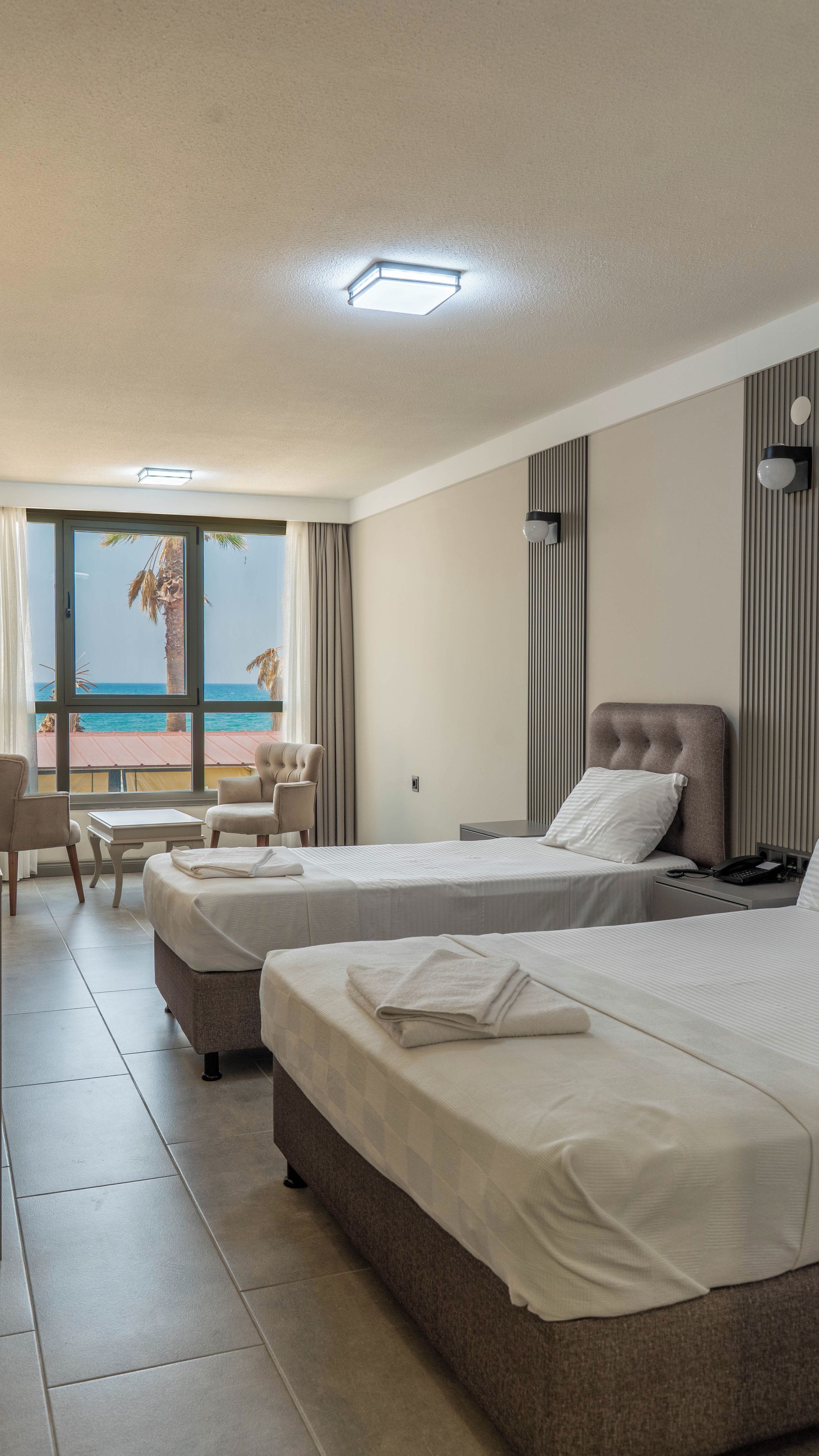 A hotel room with two beds, a seating area with a table and chairs, and a view of the ocean.