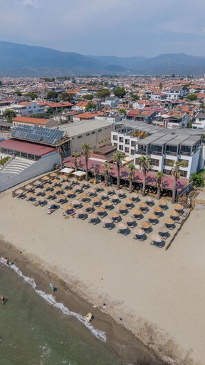 An aerial view of a coastal hotel with a beach area, multiple buildings, and a mountainous backdrop. - Grand Cennet Beach Hotel (Edremit)