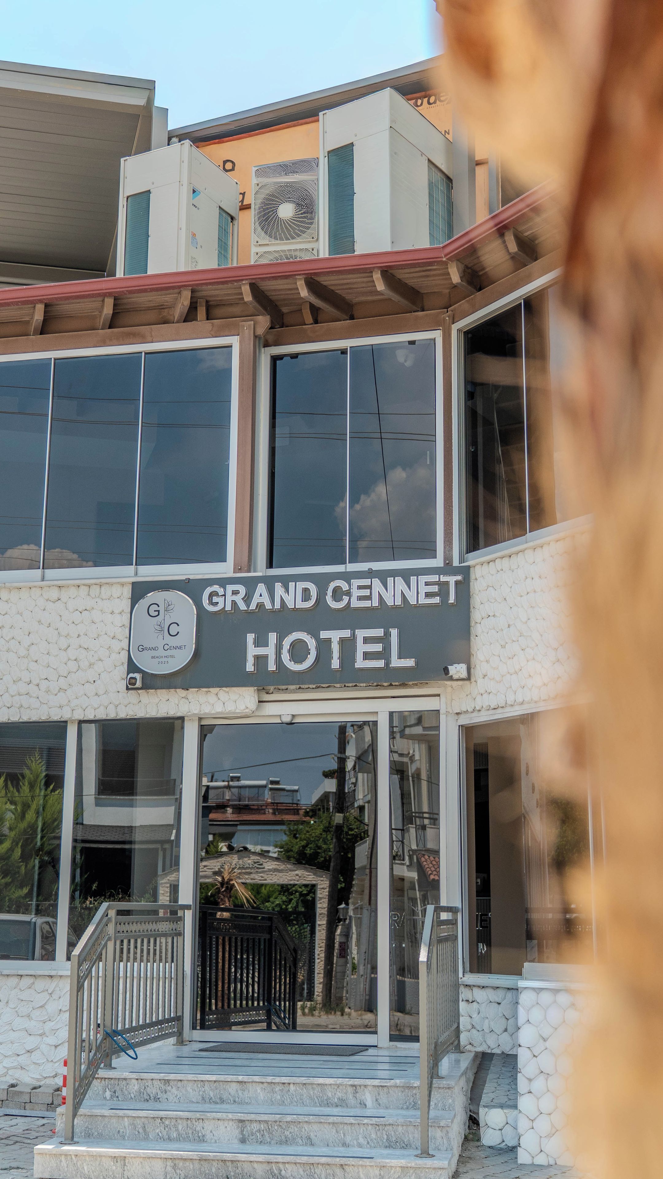 The exterior of the Grand Cennet Hotel with a clear view of the entrance, a staircase leading up to the entrance, and a signboard displaying the hotel's name.