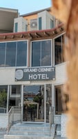 El exterior del Grand Cennet Hotel, con vista despejada a la entrada, una escalera que conduce hasta ella y un cartel con el nombre del hotel.