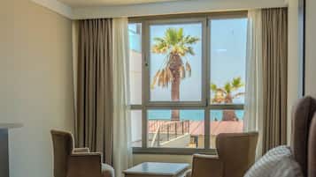 A hotel room with a bed, two chairs, a small table, and a window with a view of palm trees and a balcony.