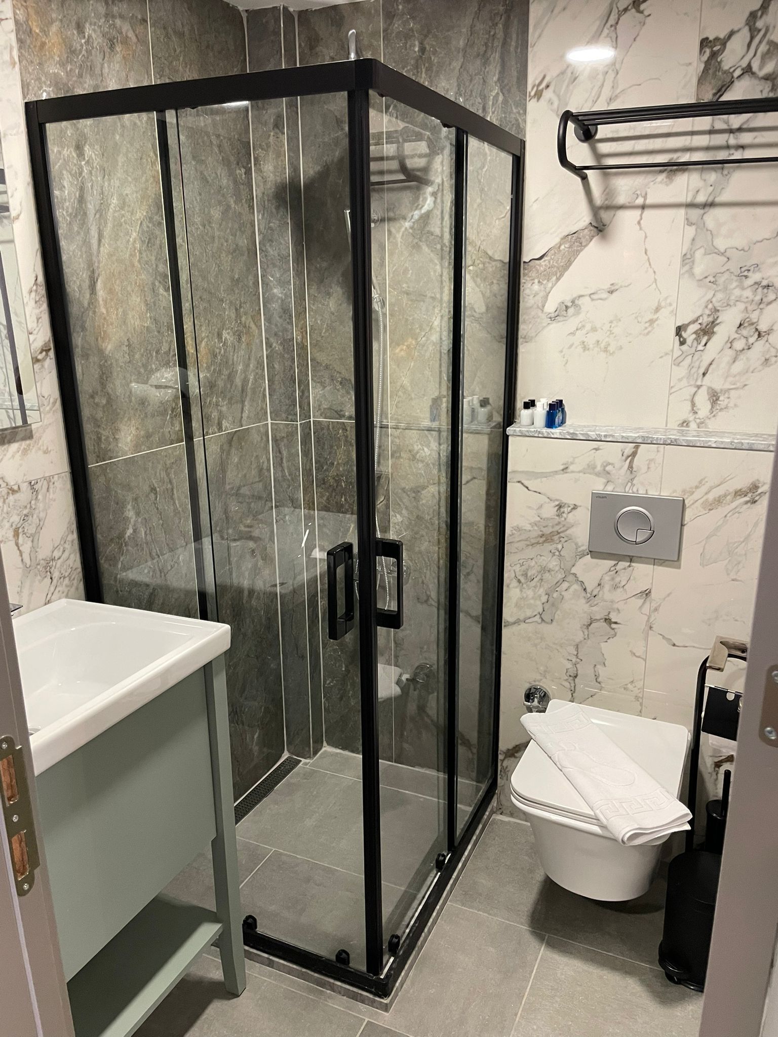 Un baño moderno con ducha de vidrio, lavamanos blanco y retrete.