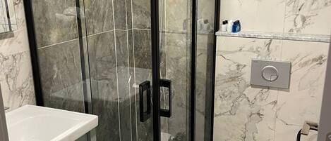 Un baño moderno con ducha de vidrio, lavamanos blanco y retrete.