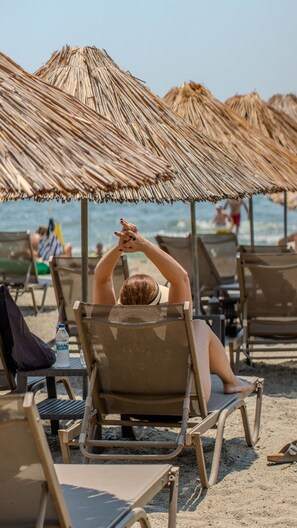 A beach scene with thatched umbrellas and lounge chairs. - Grand Cennet Beach Hotel (Edremit)