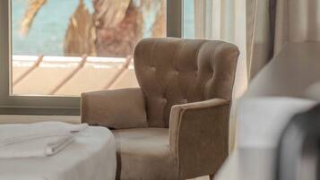 A hotel room with a bed, a chair, a view of the beach, and curtains.