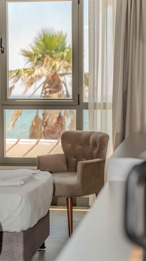 A hotel room with a bed, a chair, a view of the beach, and curtains. - Grand Cennet Beach Hotel (Edremit)