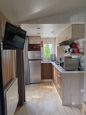 A modern kitchen with a built-in TV, stainless steel appliances, and a view of greenery outside. - Attractive fully-equipped mobile home sleeps 4 (Samoëns)