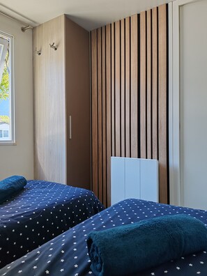 A bedroom with two beds, a wooden slat wall, and a window. - Attractive fully-equipped mobile home sleeps 4 (Samoëns)