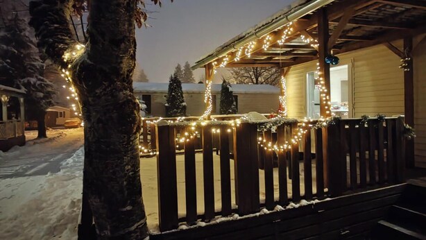 Un porche cubierto de nieve con luces colgantes y una valla de madera.