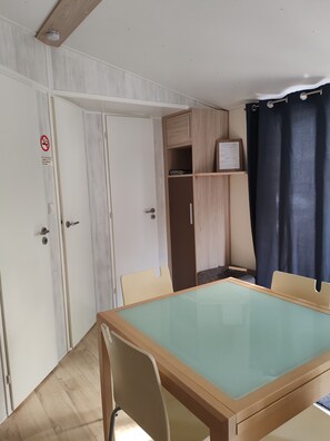 A room with a wooden table, chairs, a wardrobe, and a curtain. - Attractive fully-equipped mobile home sleeps 4 (Samoëns)