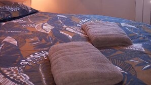Un dormitorio con cama, una ventana con cortinas, una lámpara de pared y vista a árboles desde afuera.