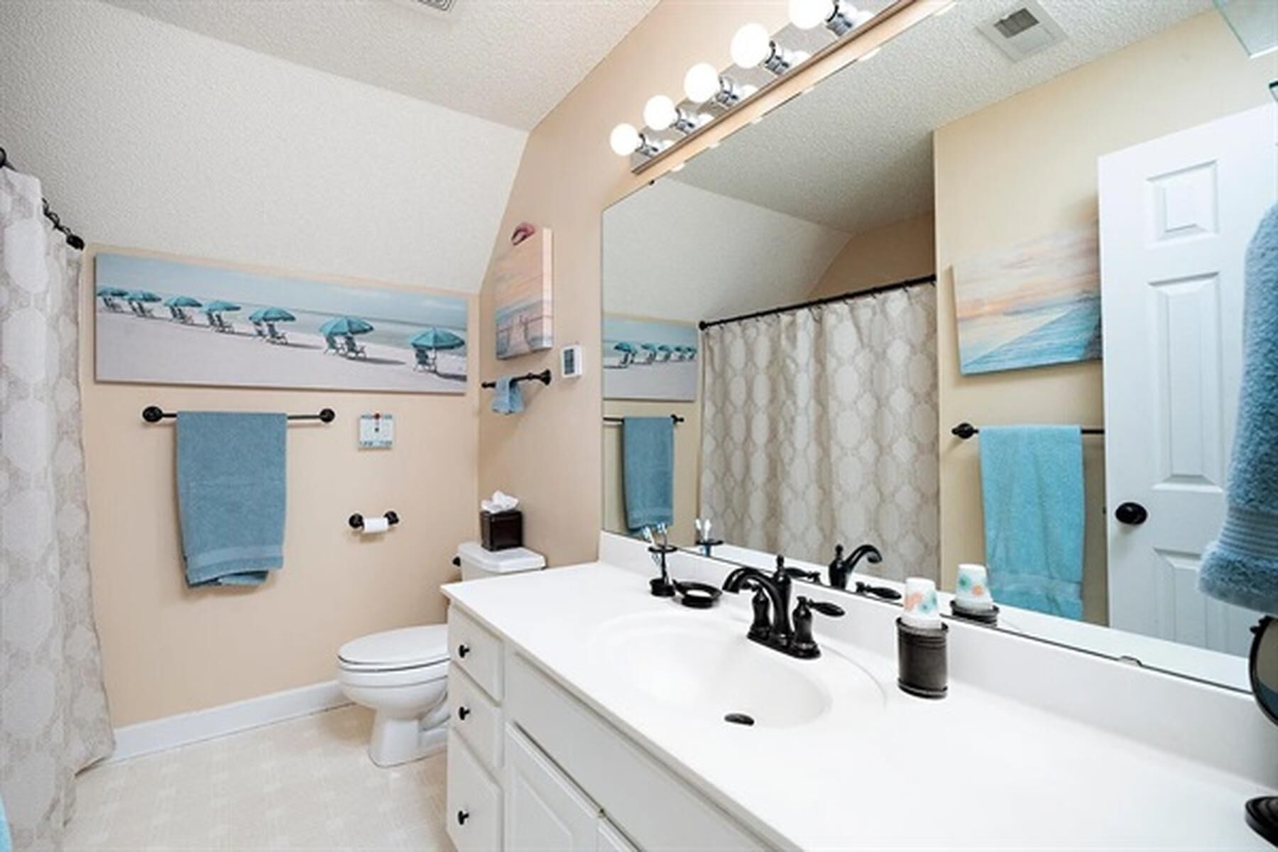 Een badkamer met een witte wastafel, een zwarte kraan en een grote spiegel met verlichting. Er is een toilet en een douchegordijn.