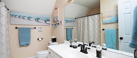 Een badkamer met een witte wastafel, een zwarte kraan en een grote spiegel met verlichting. Er is een toilet en een douchegordijn.