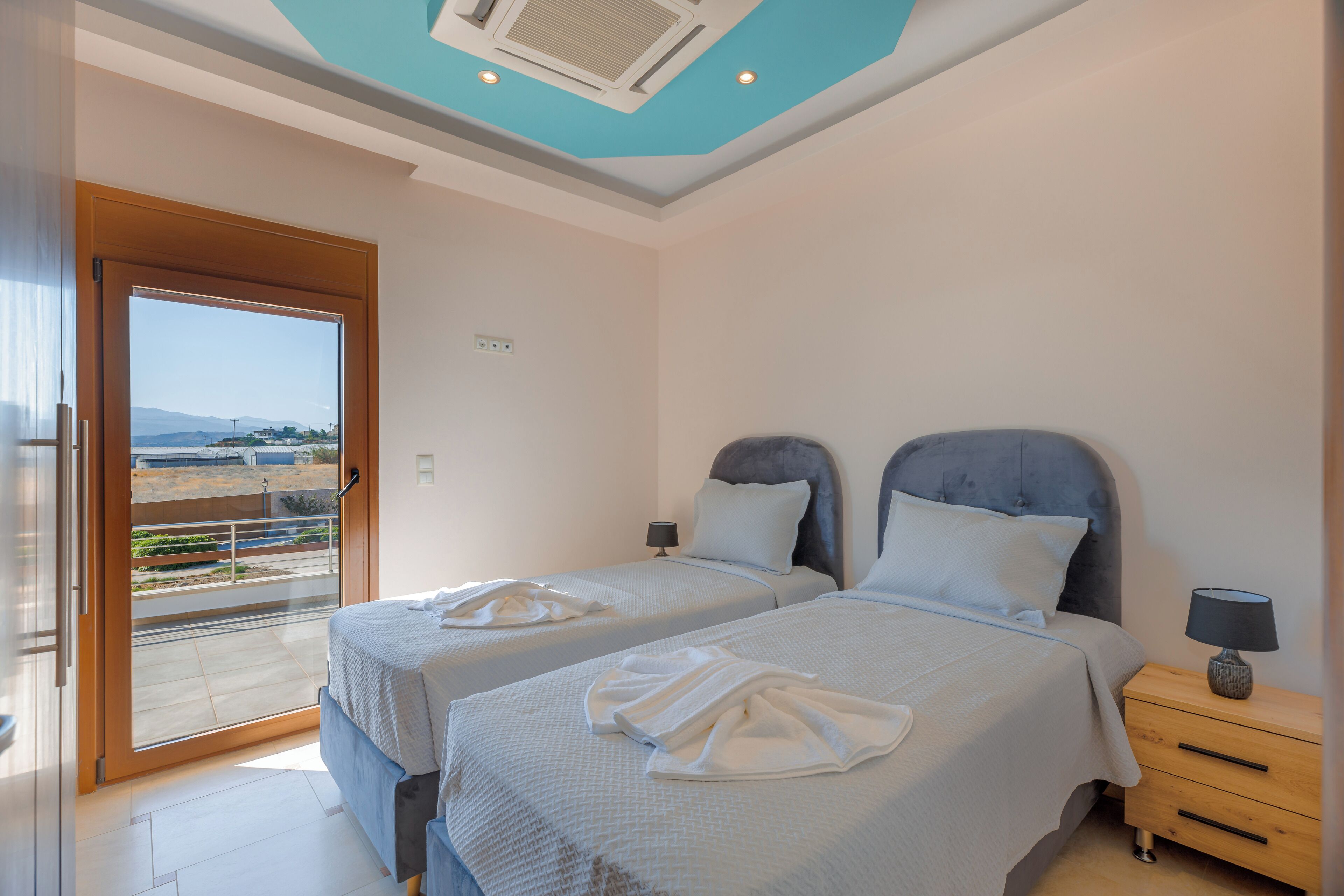 A bedroom with two beds, a balcony, and a view of the landscape.