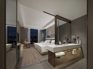 Ett modernt hotellrum med en stor säng, ett skrivbord, ett badrum med handfat och utsikt över staden.