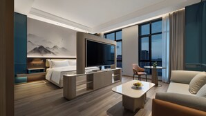 Una habitación de hotel moderna con una cama grande, un televisor de pantalla plana, una mesa de comedor con un frutero y un sofá.
