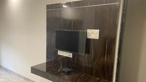 Un téléviseur fixé au mur, avec un panneau en bois en arrière-plan, une prise de courant et un boîtier pour organiser les câbles.