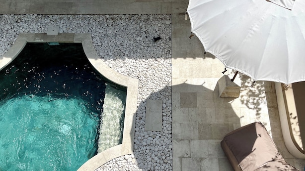 A swimming pool with a pebble border, a white umbrella, and a cushioned seating area. - Charming Two Bedroom Villa Near Seminyak (Seminyak)