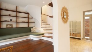 A modern interior with a curved staircase, a green cushioned bench, wooden flooring, and a white wall with a decorative mirror. - Charming Two Bedroom Villa Near Seminyak (Seminyak)