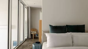 A hotel room with a large window, a bed with white and dark green pillows, a small wooden chair, and a blue side table. - Chic Seddon Retreat Near the CBD (Seddon)