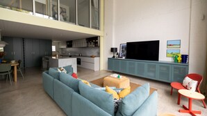 A modern living room with a large blue sofa, a small table, and a TV on a teal cabinet. - Chic Seddon Retreat Near the CBD (Seddon)