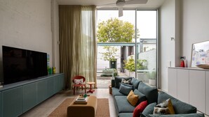 A modern living room with a flat-screen TV, a sofa set, a red chair, and a small table. - Chic Seddon Retreat Near the CBD (Seddon)