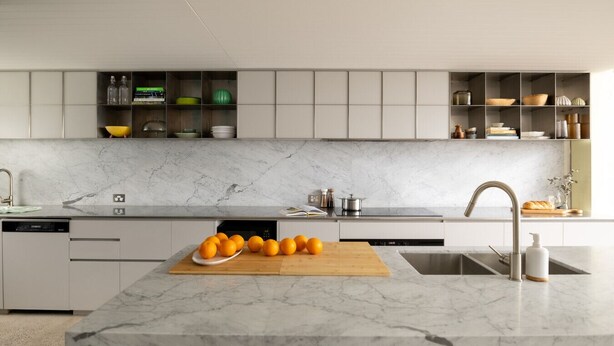 A modern kitchen with a marble countertop, built-in cabinets, and a central island with oranges. - Chic Seddon Retreat Near the CBD (Seddon)