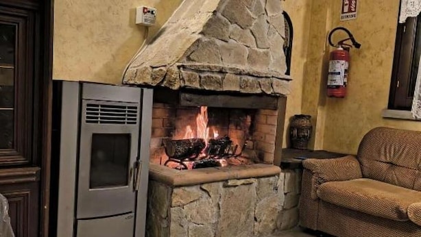 A stone fireplace with a fire burning, a modern refrigerator, and a wicker sofa in a cozy room.