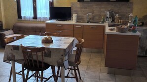 A dining area with a table, chairs, and a sofa. A kitchen area with a stove, sink, and cabinets is visible in the background.