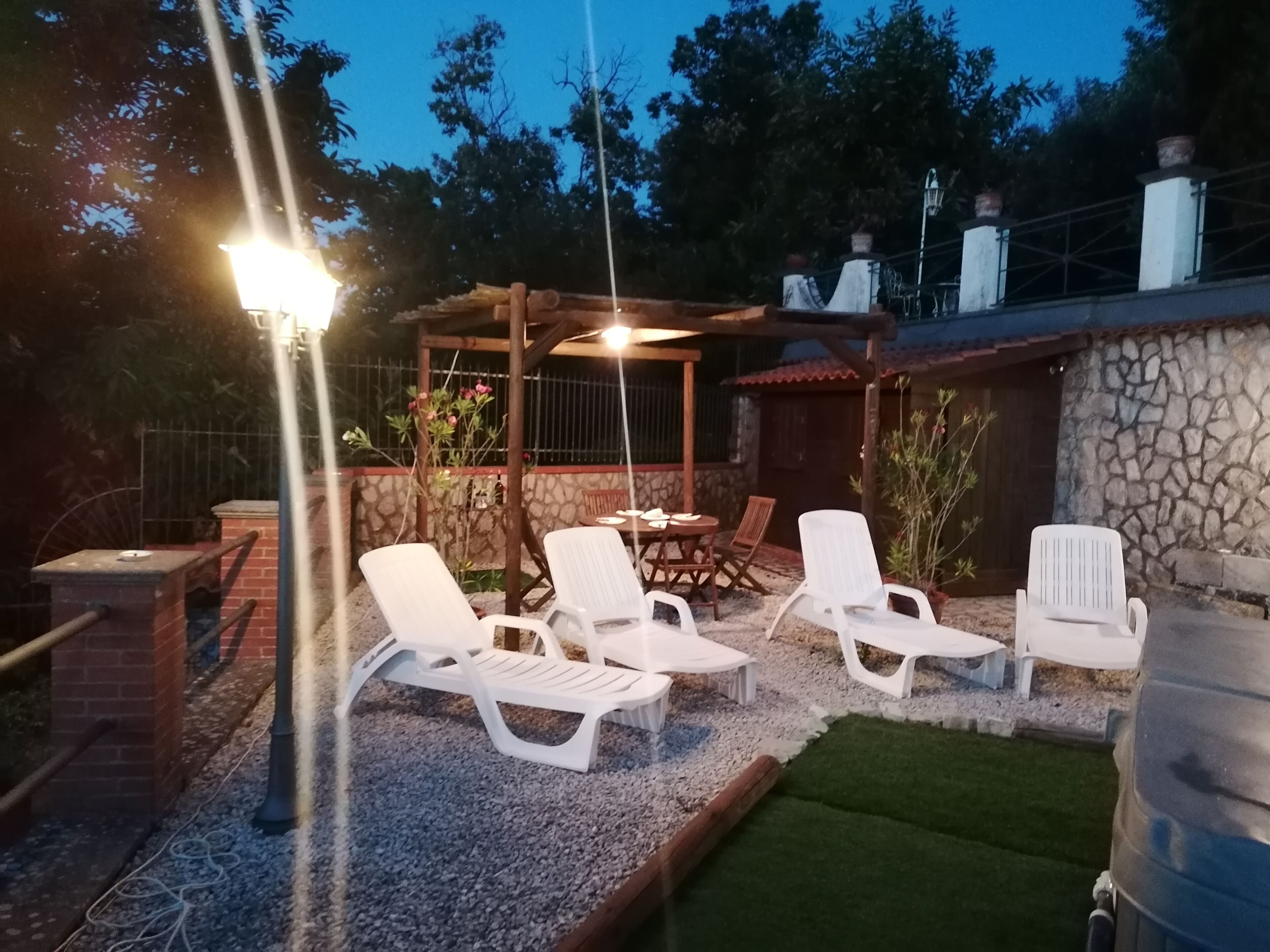 Een terras met witte loungestoelen, een tafel en een pergola met verlichting.