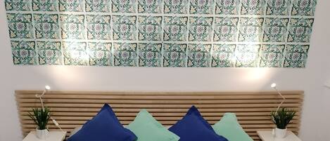 Un dormitorio ordenado con una pared estampada, una cama con cubrecama color beige y dos mesitas de noche con lámparas y plantas.