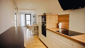 A modern kitchen with a wooden countertop, built-in oven, and a dining area with a table and chairs. - Le Wilson - Modern, comfortable duplex (Vannes)