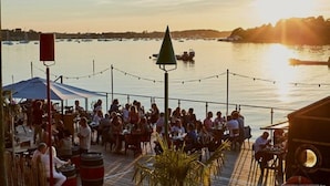 A waterfront restaurant with outdoor seating, a view of the water, and a sunset in the background. - Le Wilson - Modern, comfortable duplex (Vannes)