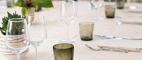 Una mesa de comedor dispuesta con copas de vino, cubiertos y una pequeña planta en maceta.