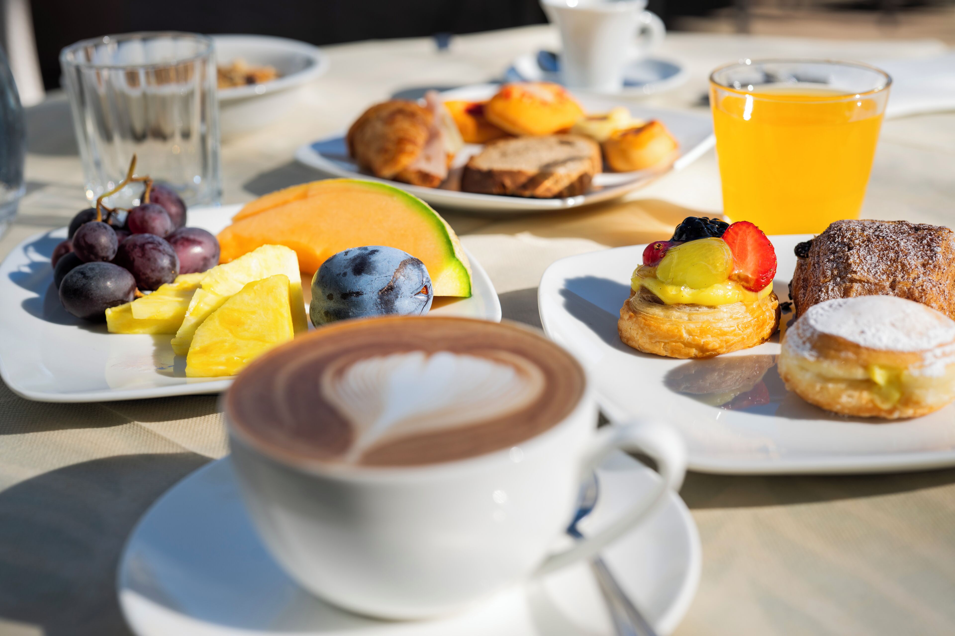 A breakfast setting with plates of fruit, pastries, and a cup of coffee.