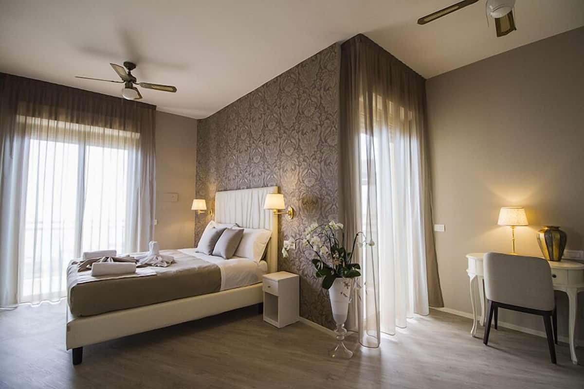 A modern hotel room with a large bed, bedside tables, a desk, and a chair.