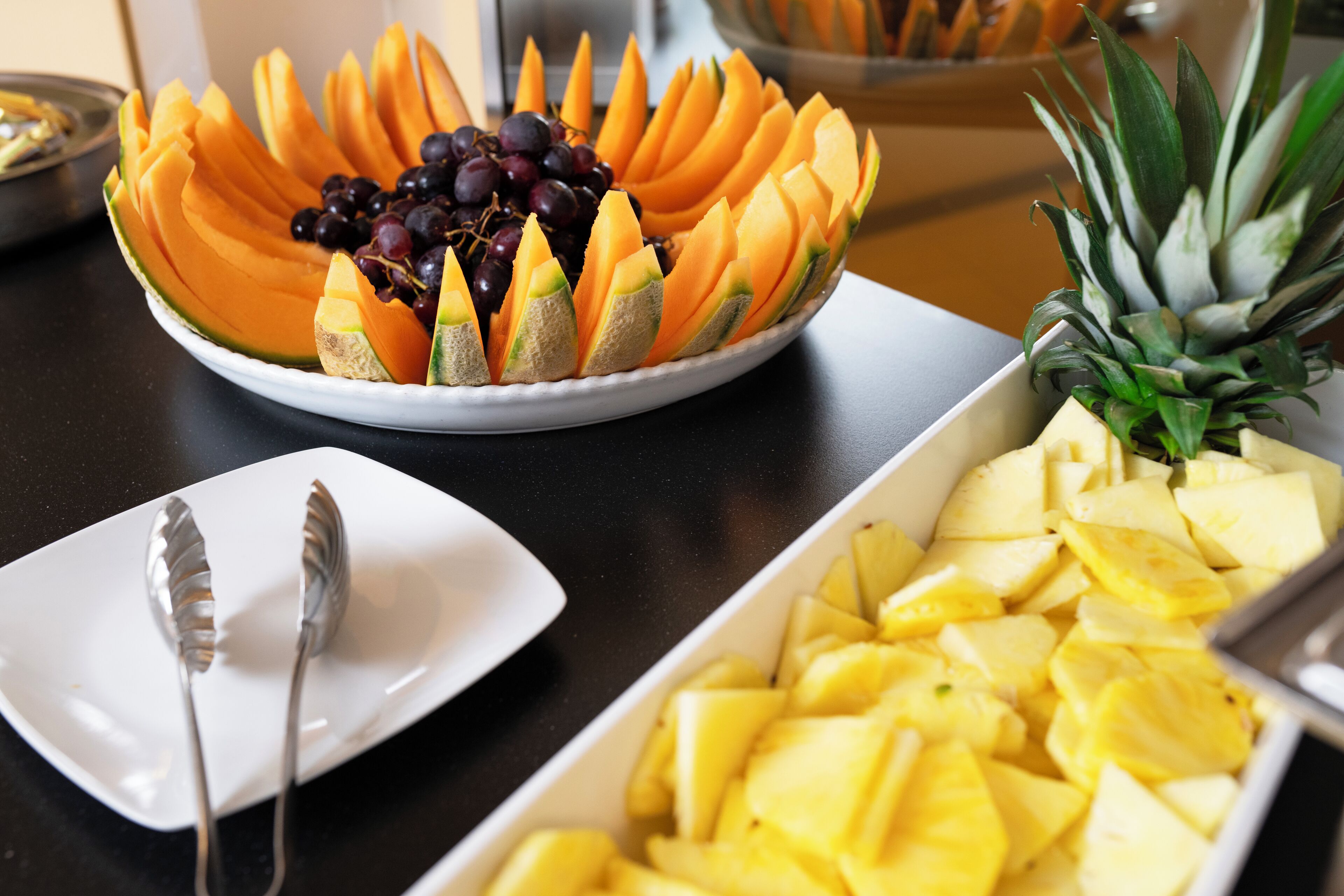 A buffet table with a variety of fruits including sliced melon, grapes, and pineapple.