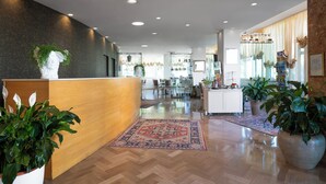 A hotel lobby with a reception desk, wooden flooring, and potted plants. - Hotel Lady Mary (Milano Marittima)