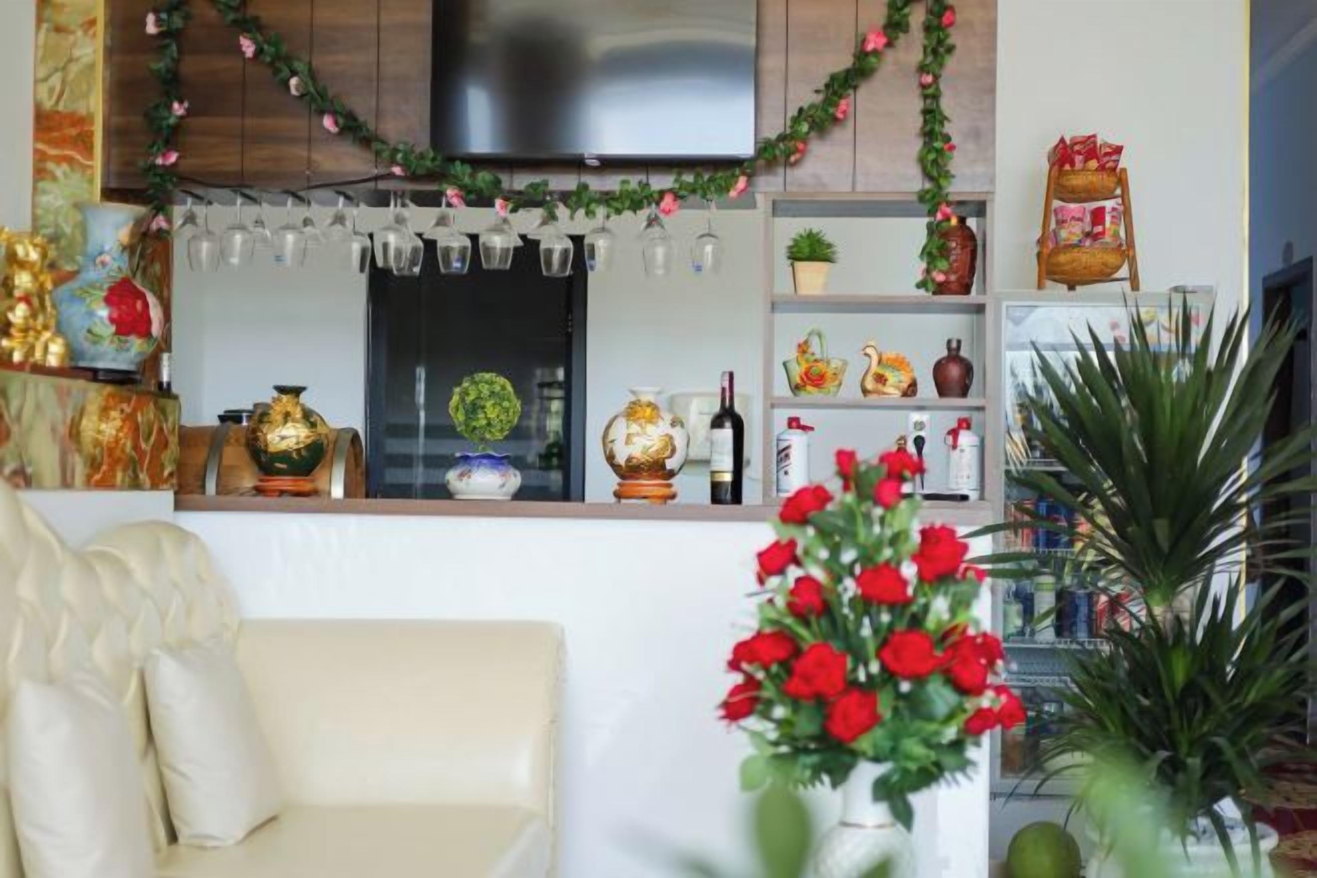 Una sala de estar con sofá, televisión y una zona de cocina con refrigerador, estantes y objetos decorativos.