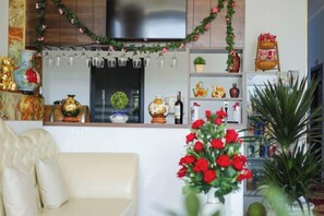 Un salon comprenant un canapé, un téléviseur et un coin cuisine avec un réfrigérateur, des étagères et des objets de décoration.