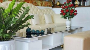 Een moderne woonkamer met een glazen salontafel, een witte bank en een beige voetenbankje.
