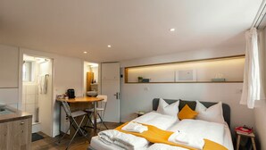 Moderni hotellihuone, jossa on sänky, työpöytä ja suihkutila.
