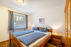 A bedroom with a wooden bed, a bedside table with a lamp, a window with curtains, and a painting on the wall. - Apartment 'Fewo Brünnstein – Room 6' with Mountain View, Shared Garden & Wi-Fi (Oberaudorf)
