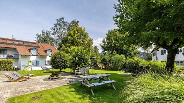 Een tuin met een picknicktafel, lounge stoelen en een kleine pergola.